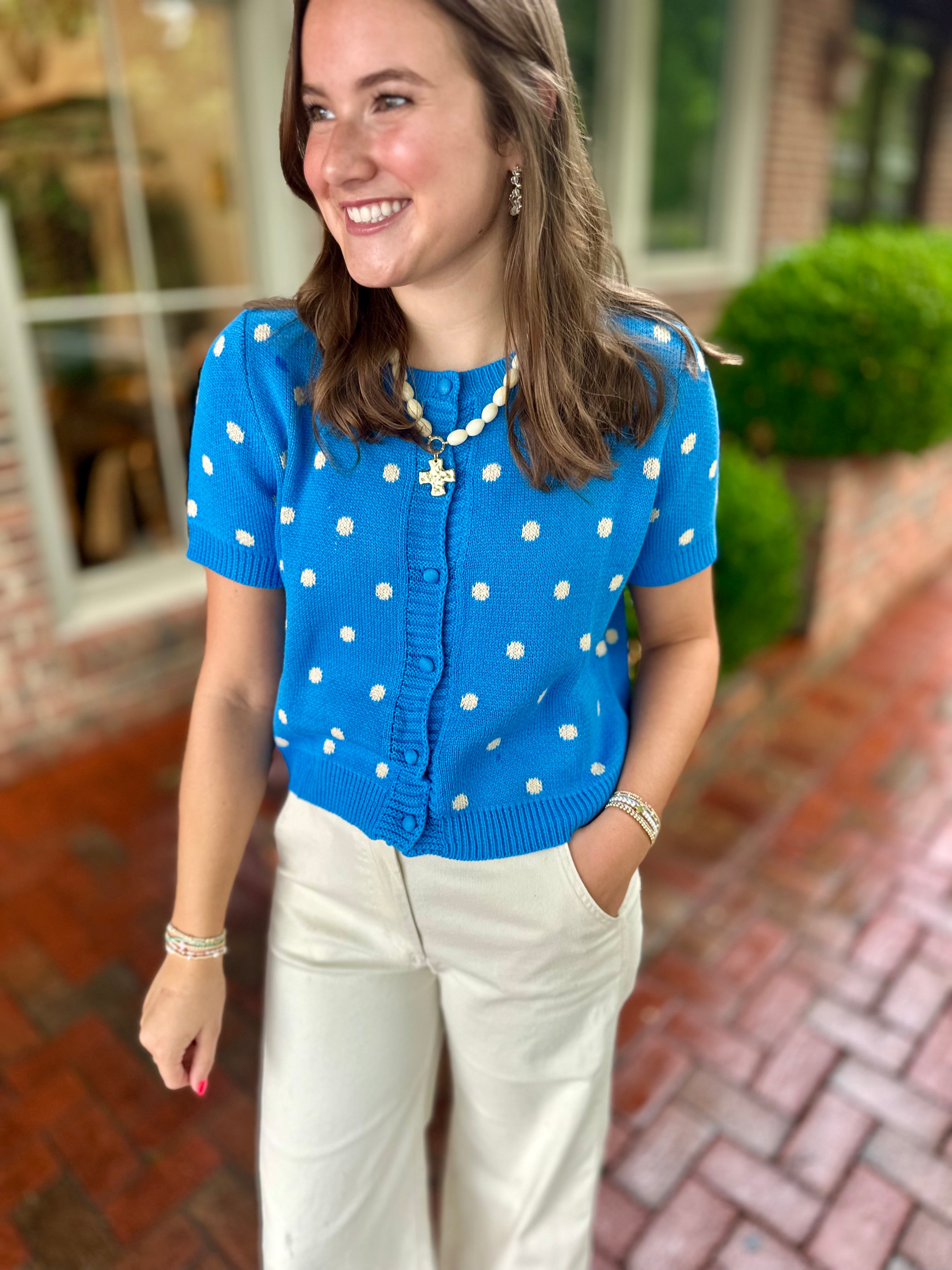 Model wearing a bright blue short-sleeve polka dot cardigan paired with cream wide leg pants from Pink Chair Boutique.