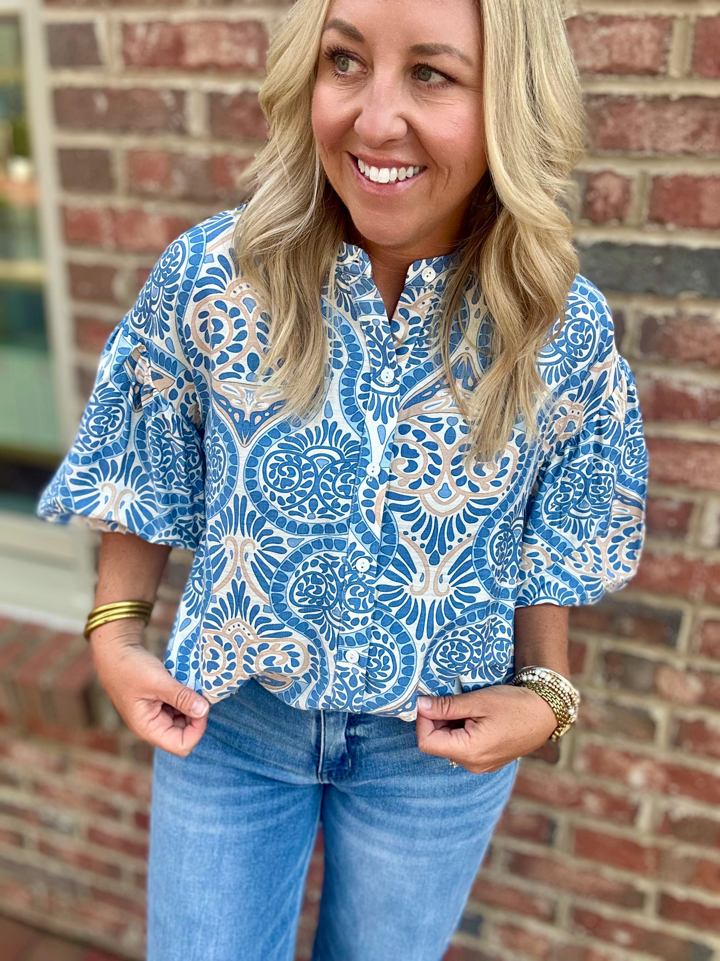 Model wearing a blue and cream printed button-down blouse with short puff sleeves and a collared neckline from Pink Chair Boutique.
