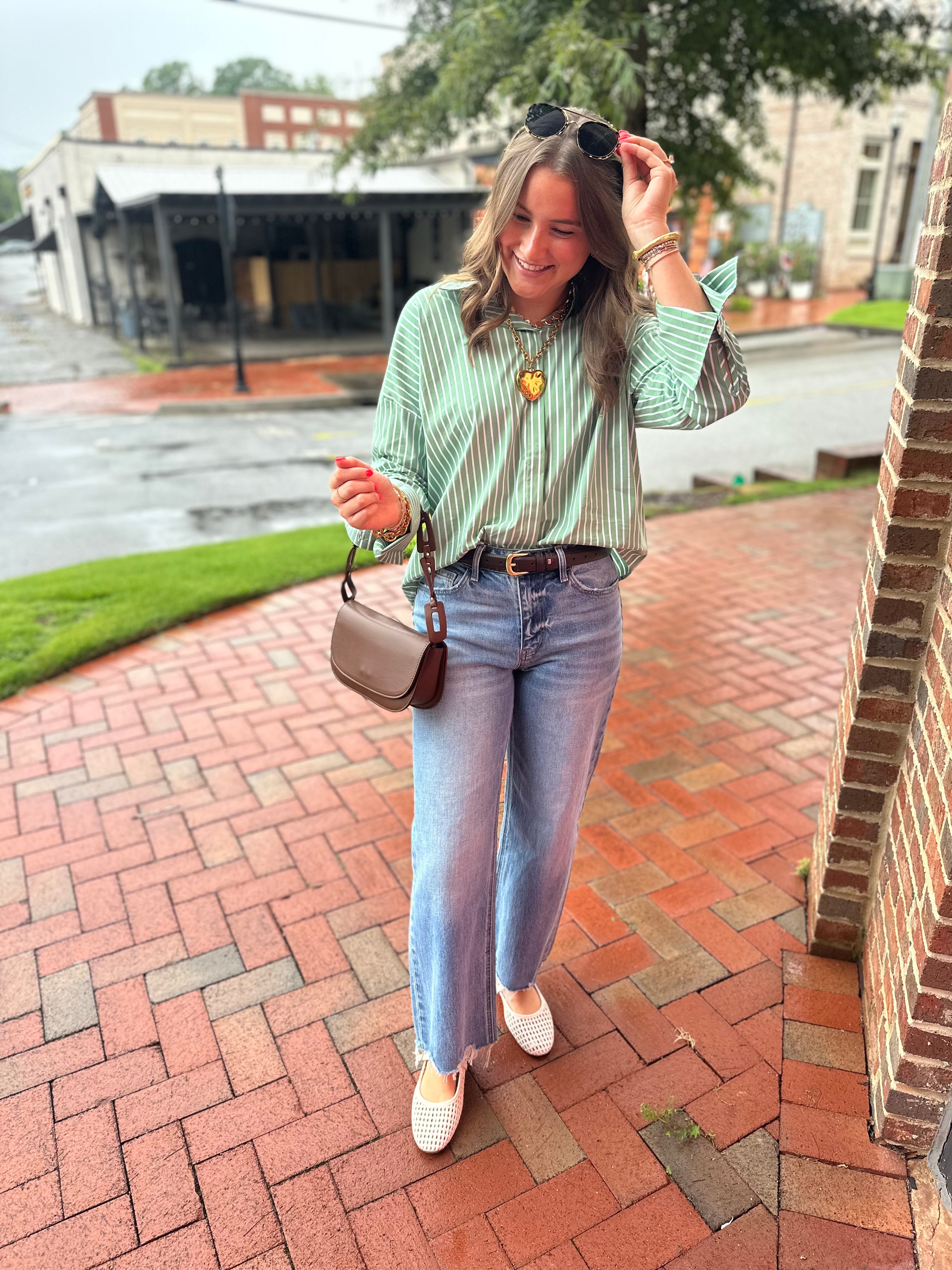 Model wearing a green and white striped button-down blouse with long sleeves styled with medium wash wide leg jeans from Pink Chair Boutique.