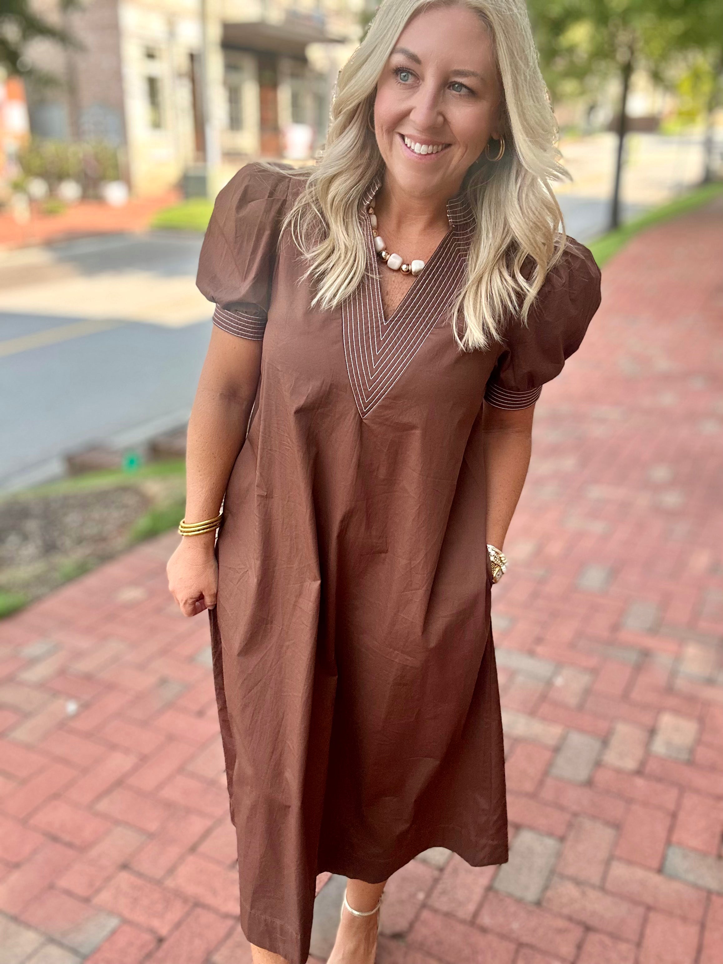 Model wearing a brown midi dress with puff sleeves, embroidered V-neckline, and a relaxed fit from Pink Chair Boutique.