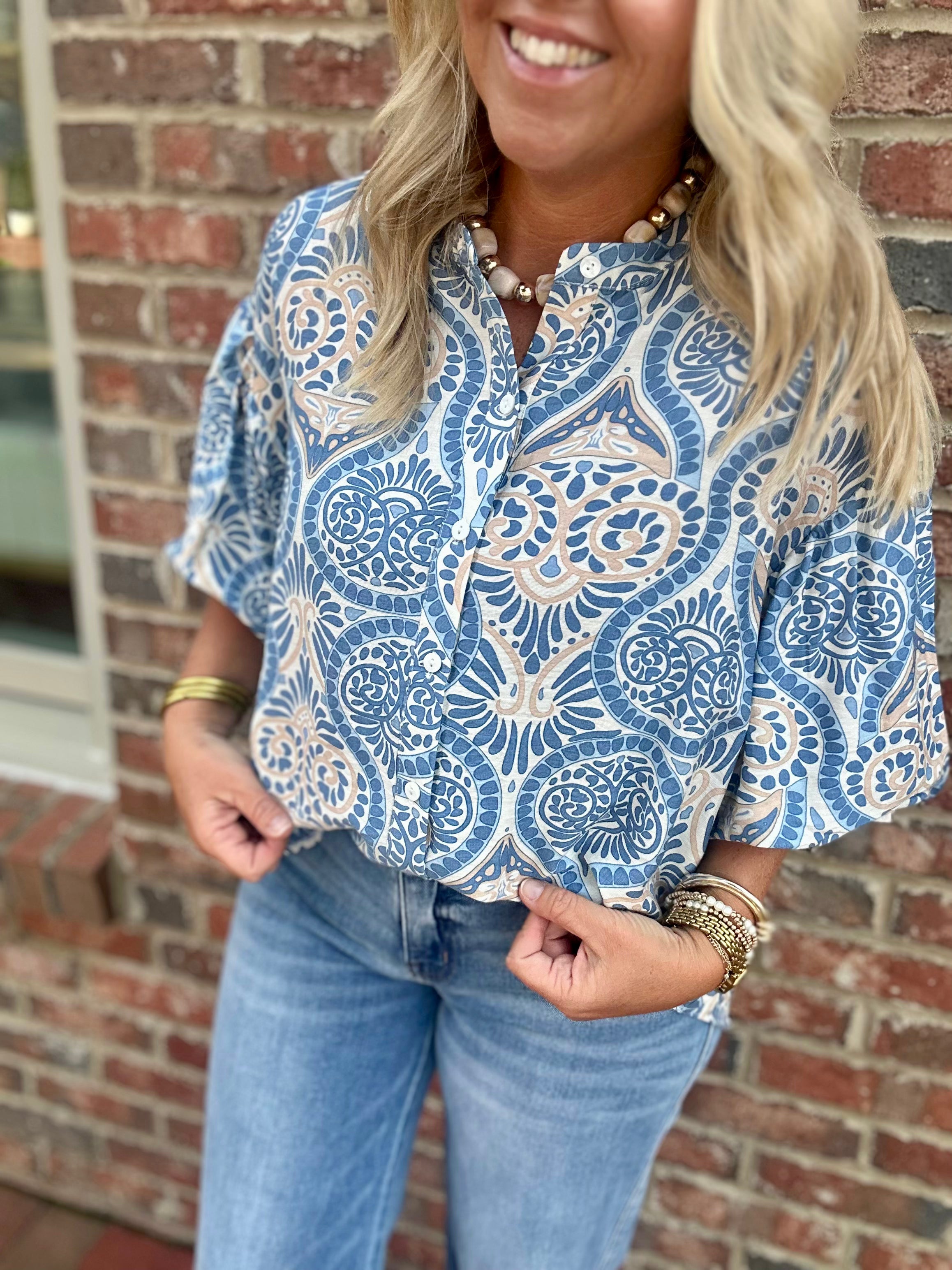 Model wearing a blue and cream printed button-down blouse with short puff sleeves and a collared neckline from Pink Chair Boutique.