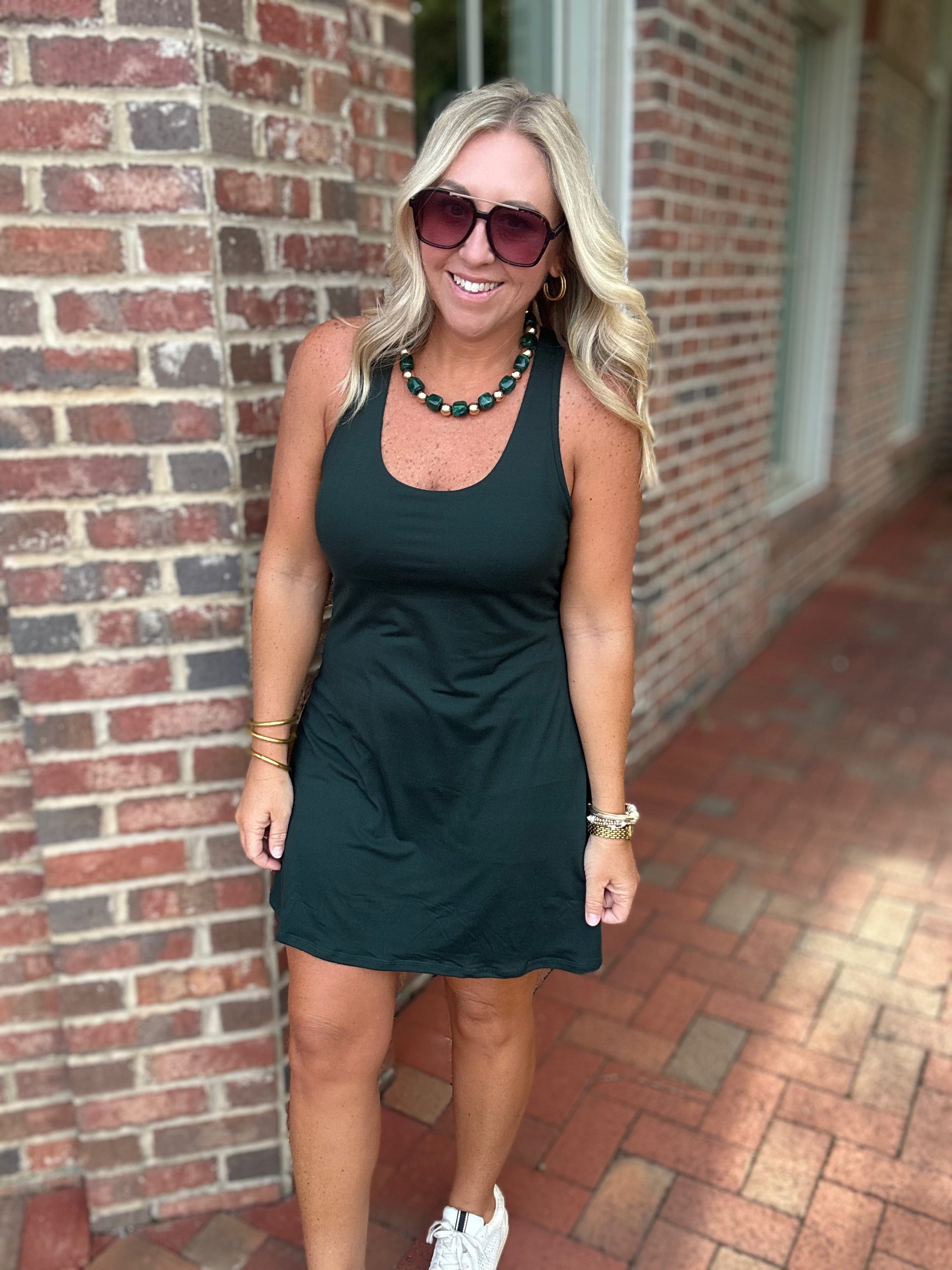 Model wearing a gree  sleeveless everyday dress styled with white sneakers, oversized sunglasses, and a green beaded necklace from Pink Chair Boutique.